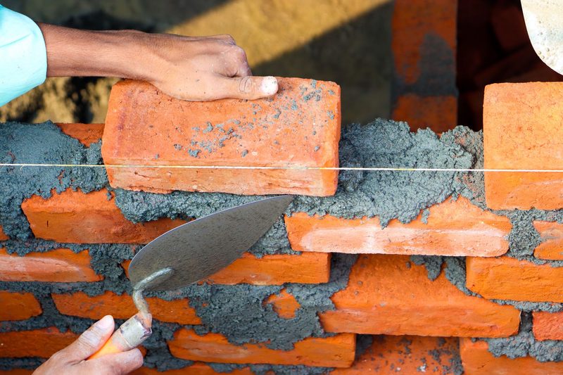 A bricklayer setting a brick on fresh mortar with a trowel