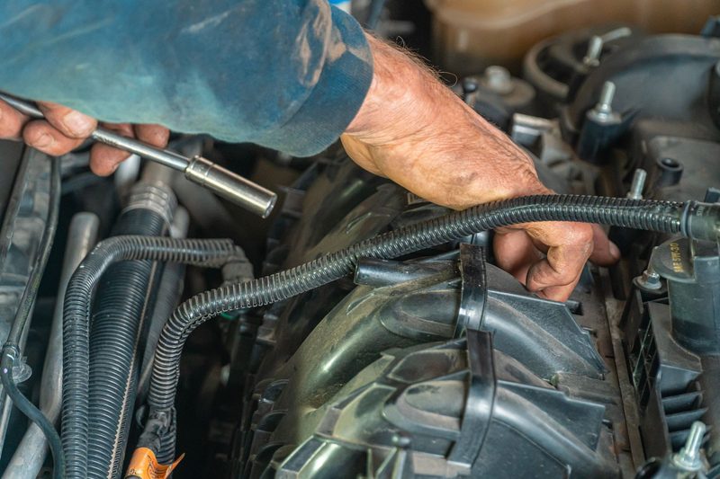 A mechanic working with a socket wrench under a bonnet