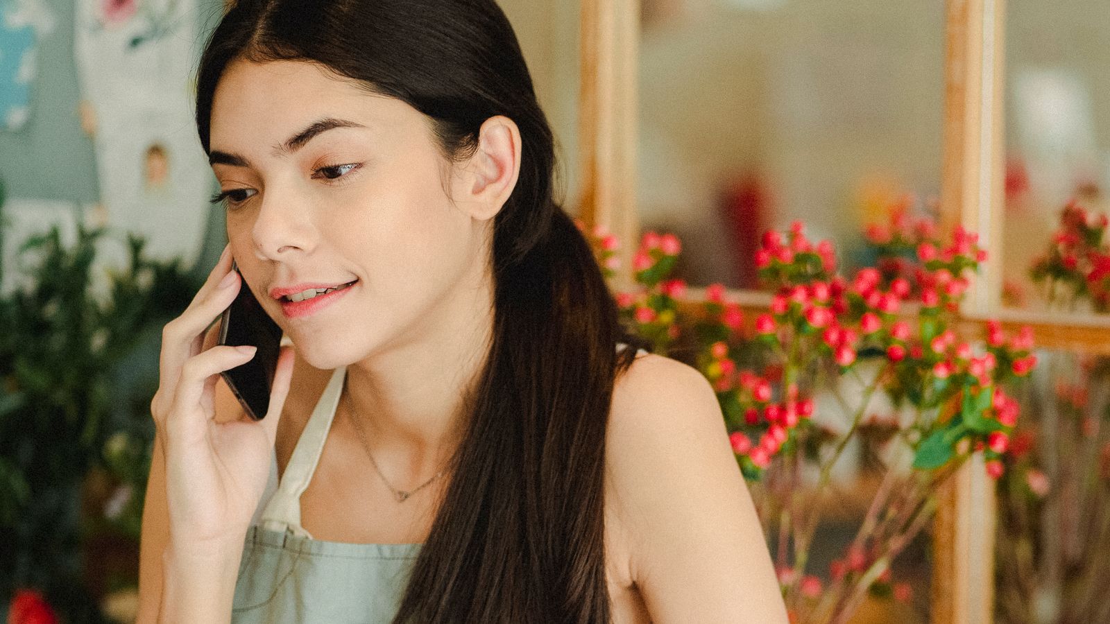 A florist in an apron talks on her phone in her flower shop.