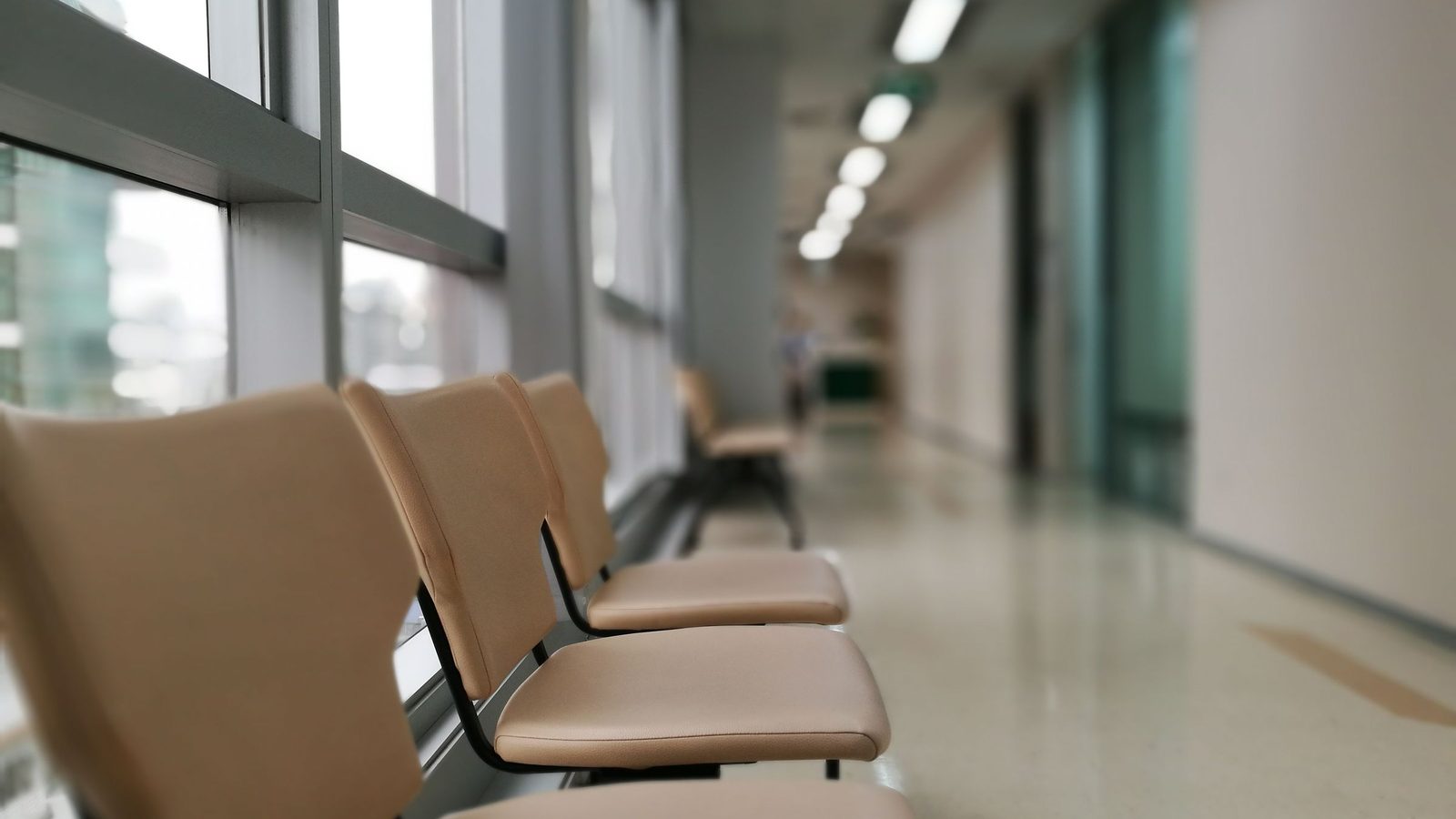 A row of empty chairs along a bright hospital corridor.