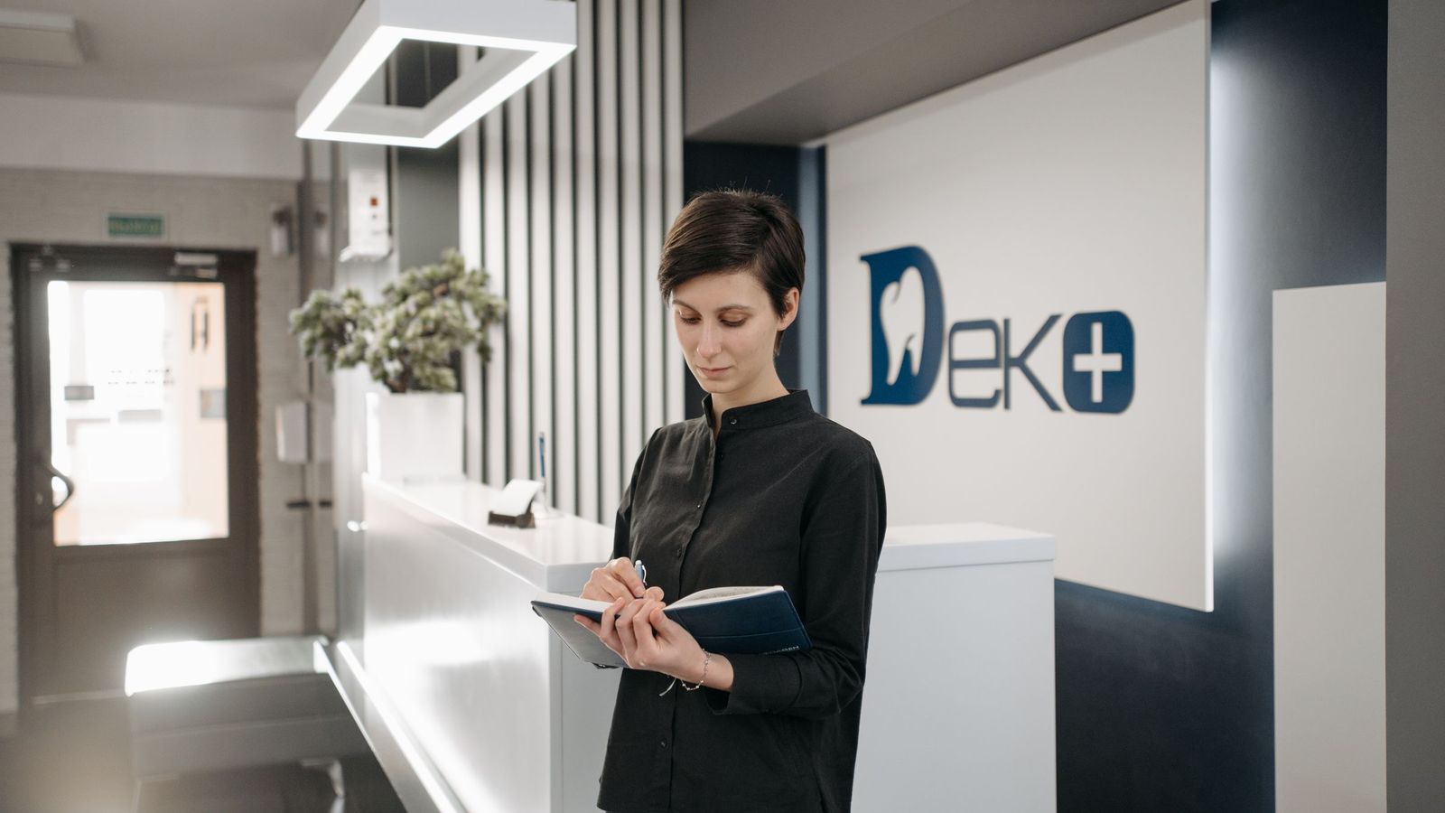 A receptionist writes notes at the front desk of a dental practice.