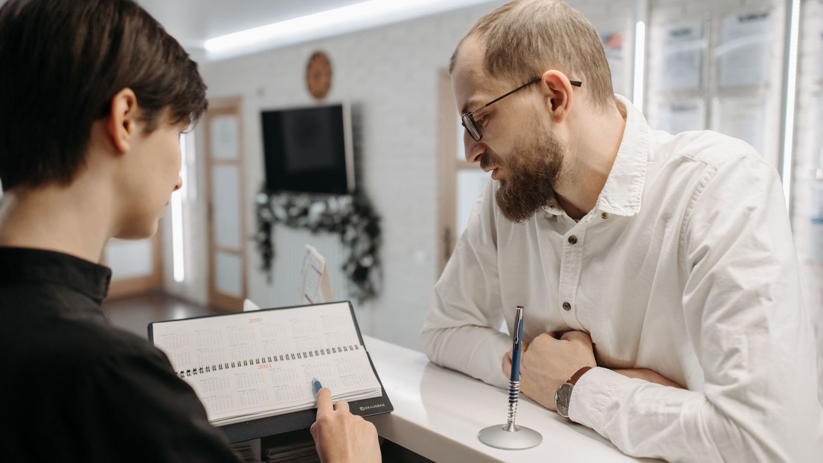 A receptionist goes through the appointment book with a patient at a dental practice front desk.