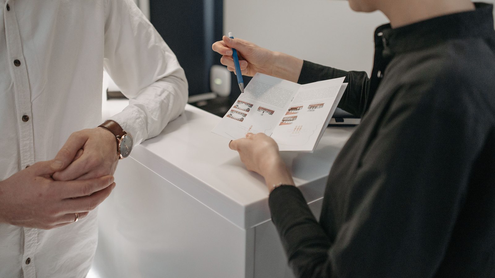 A receptionist shows a leaflet to a man at a practice reception desk.