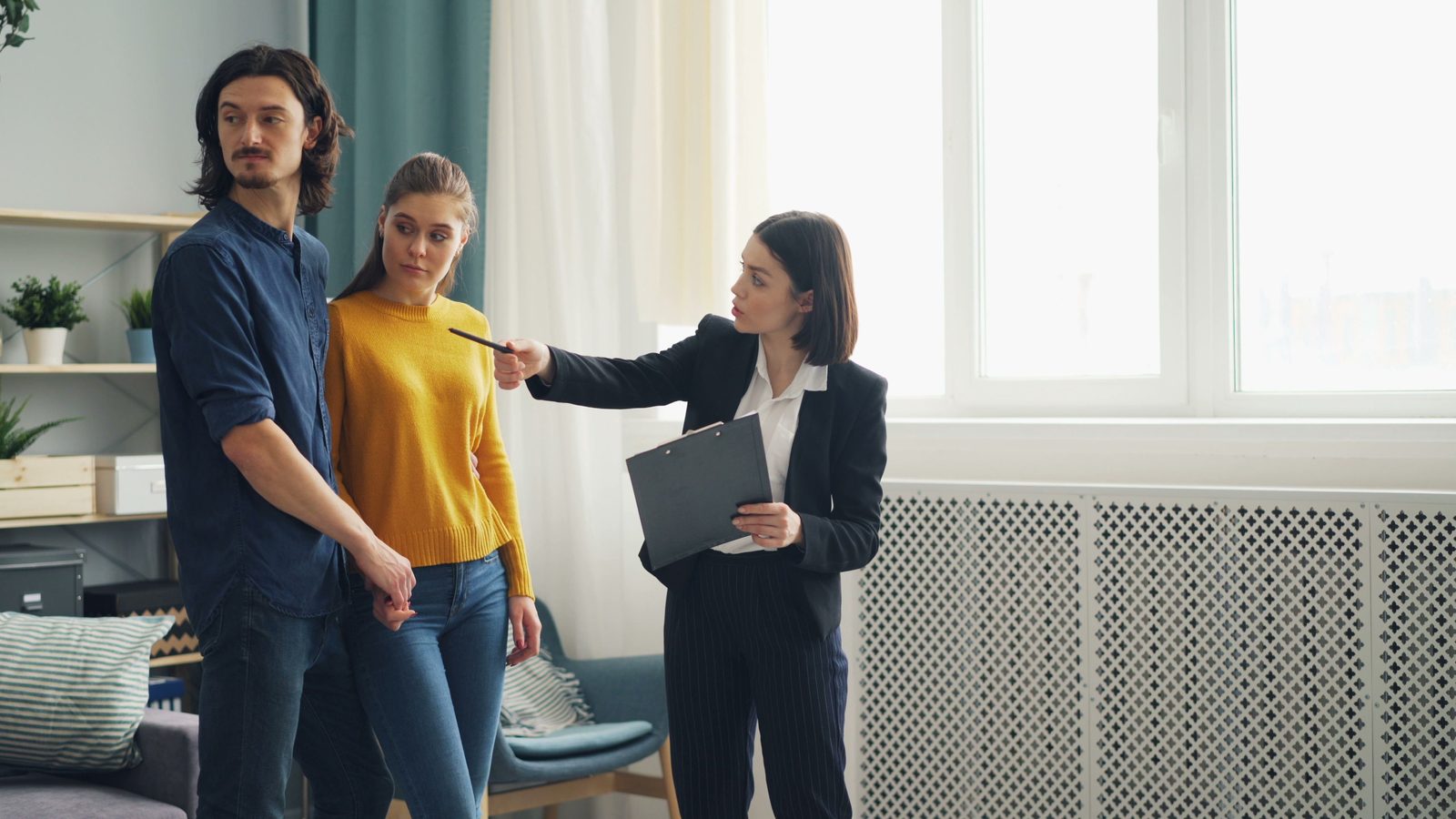 An estate agent with a clipboard shows a couple round a home.