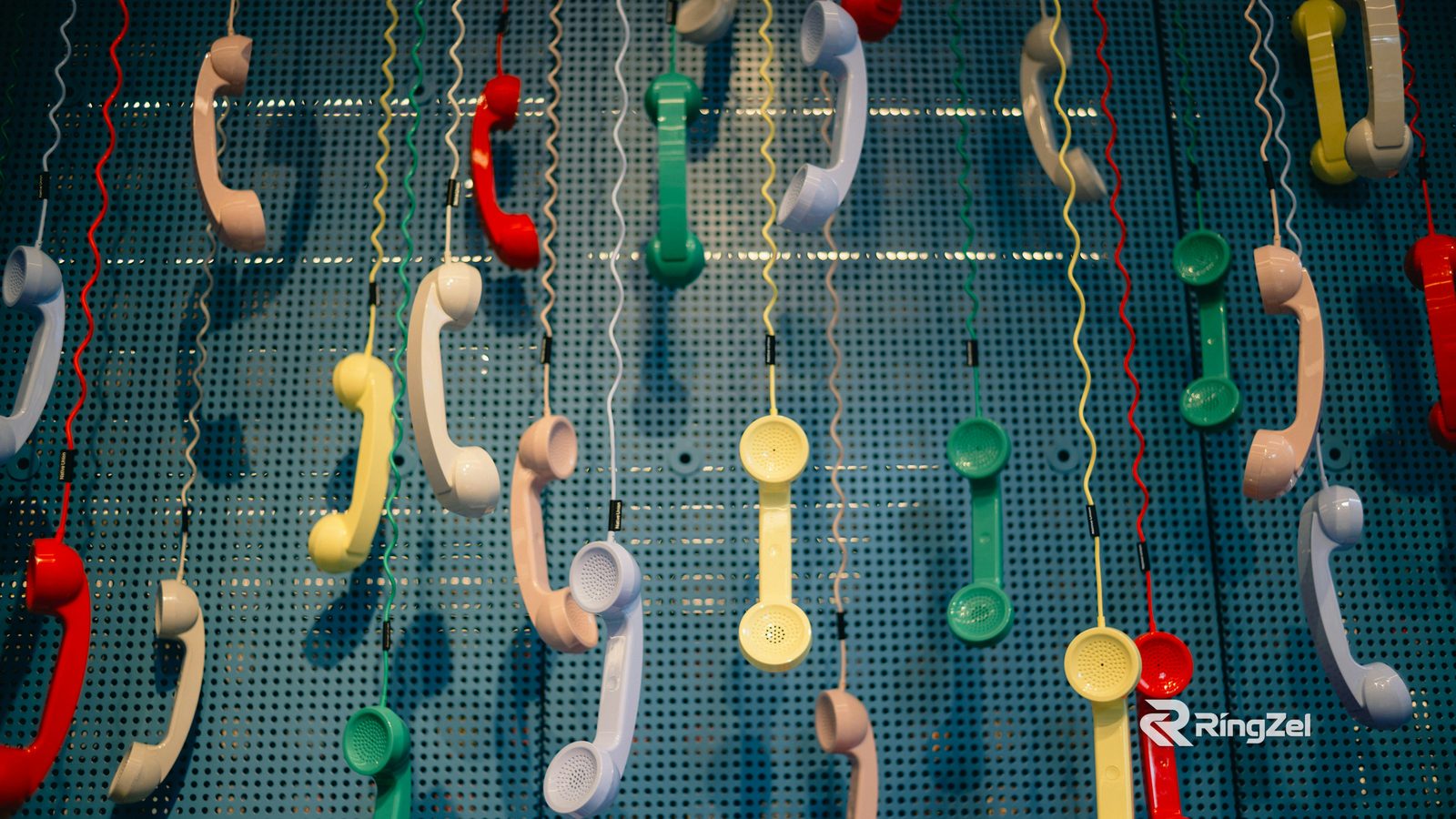 Dozens of colourful telephone handsets hanging on coiled cords against a blue pegboard wall.