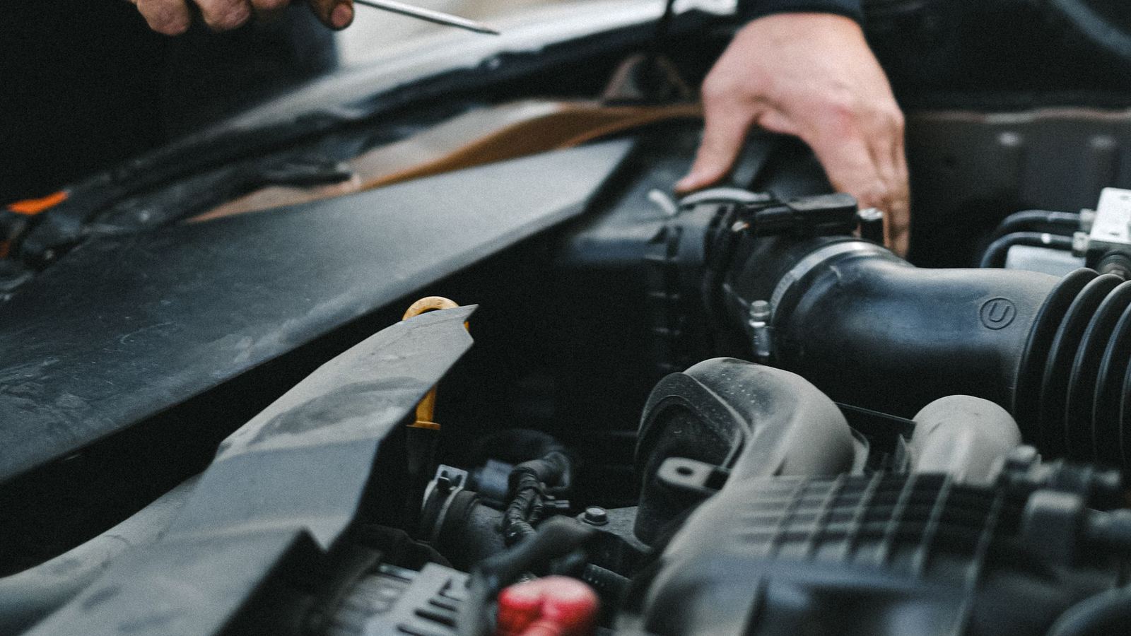 A mechanic leans over an open car bonnet, checking the engine with a tool in hand.