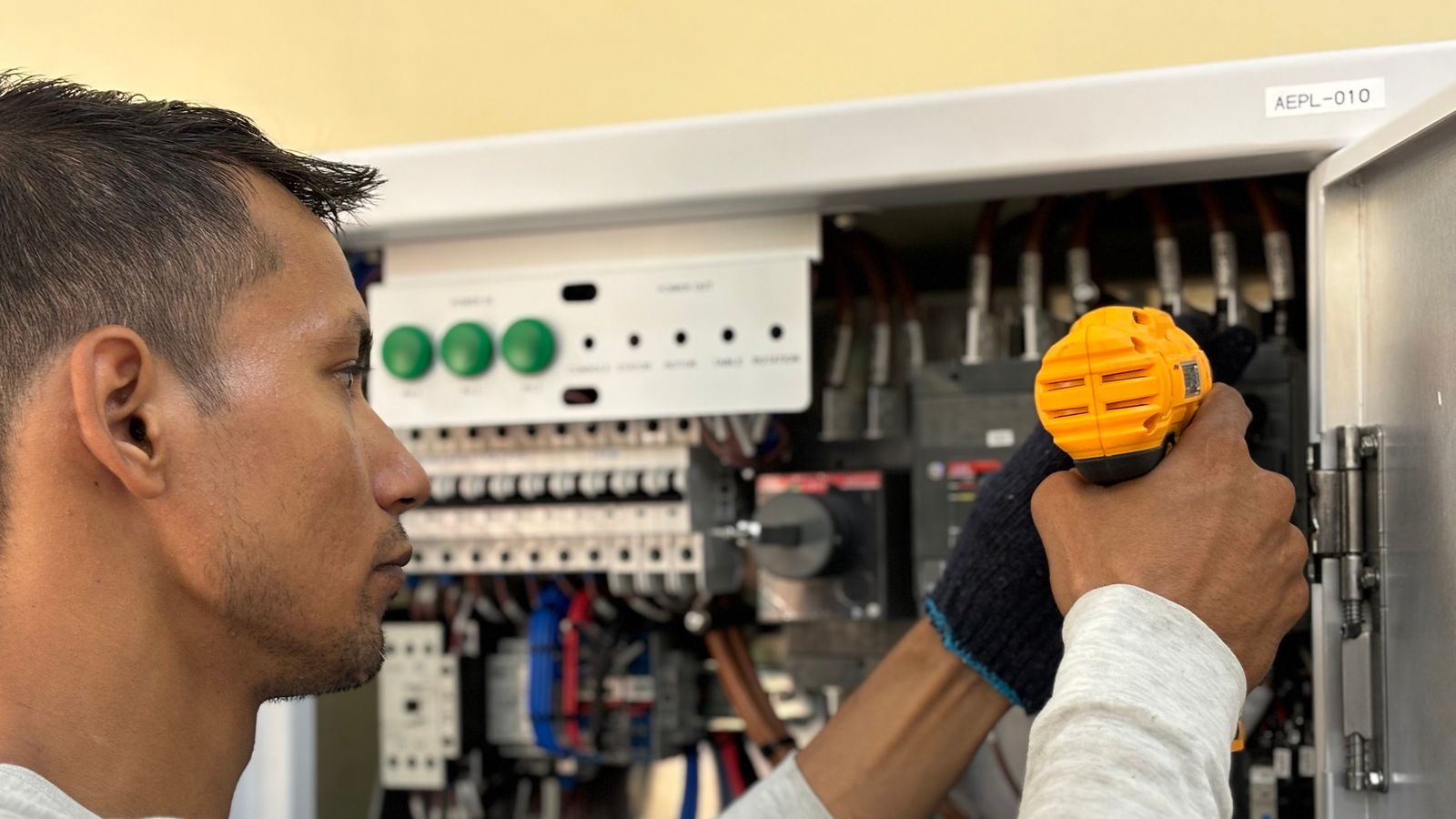 An electrician uses a cordless drill on an open distribution board full of breakers and wiring.