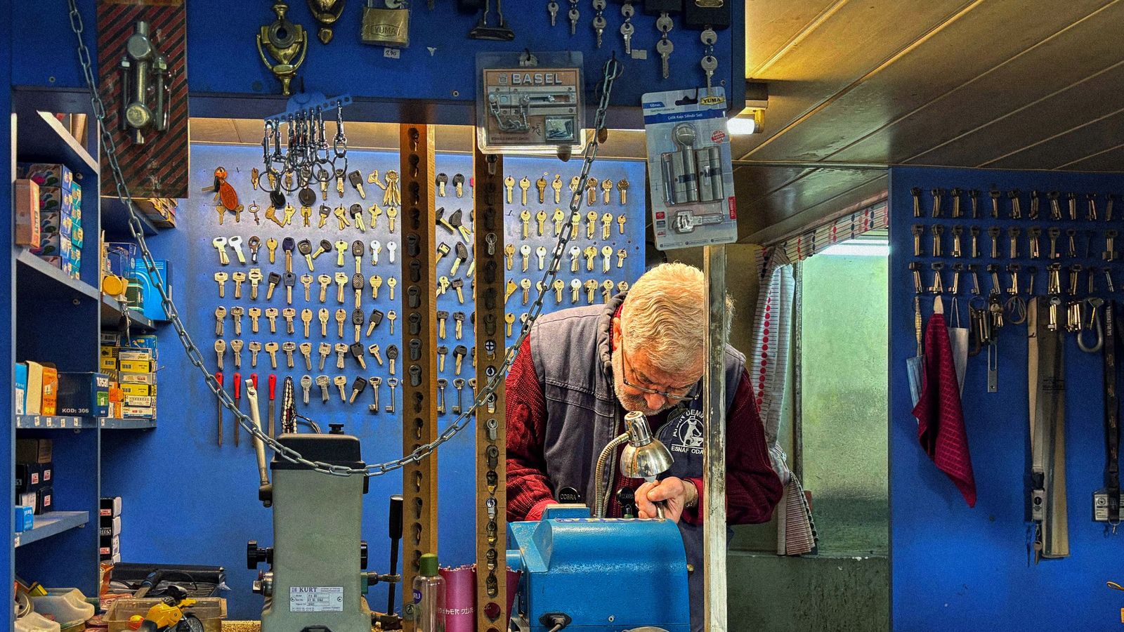 A locksmith in glasses cuts a key at a machine in a small shop lined with blank keys and padlocks.