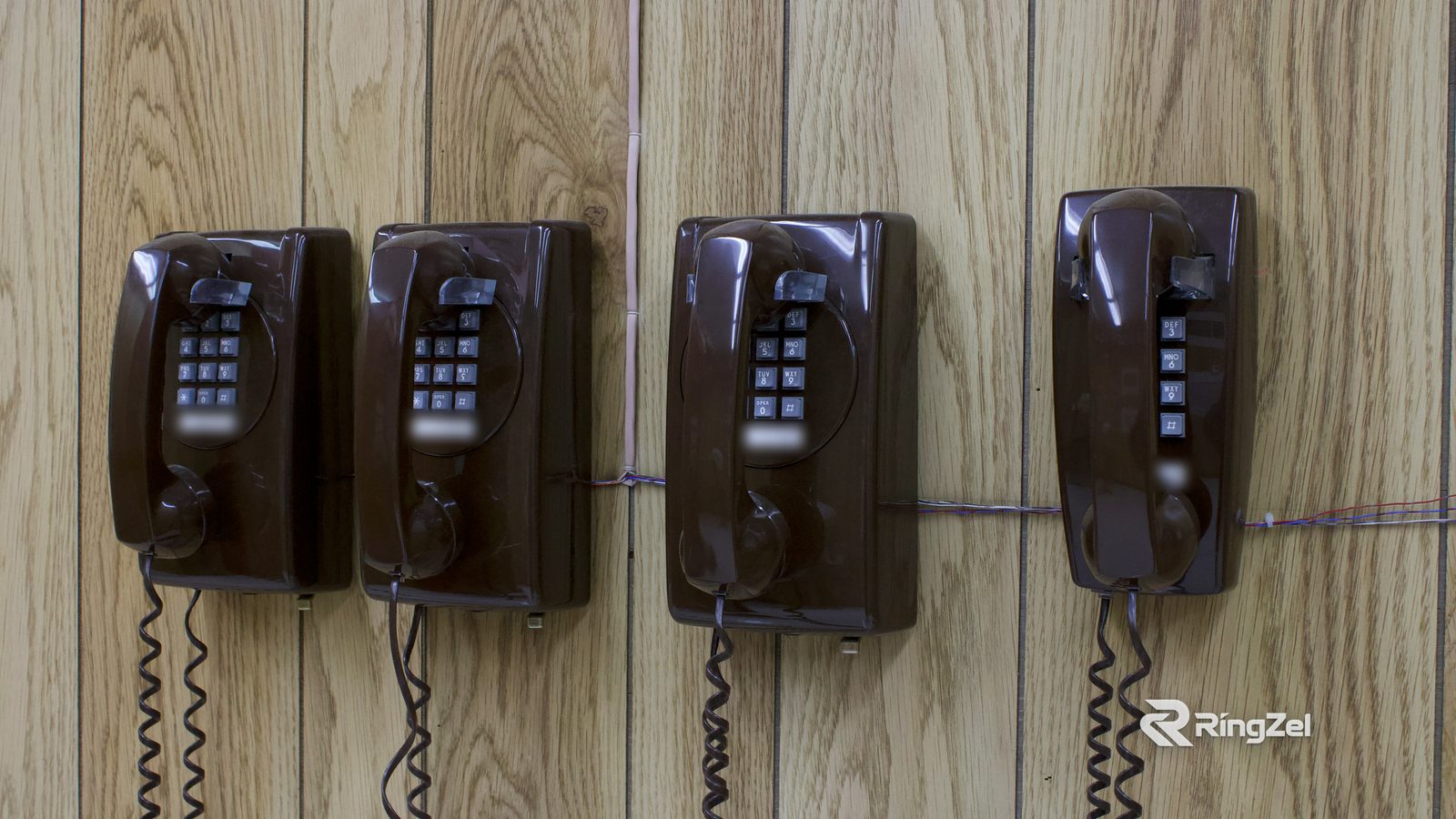 Four brown wall-mounted landline phones in a row on a wood-panelled wall.