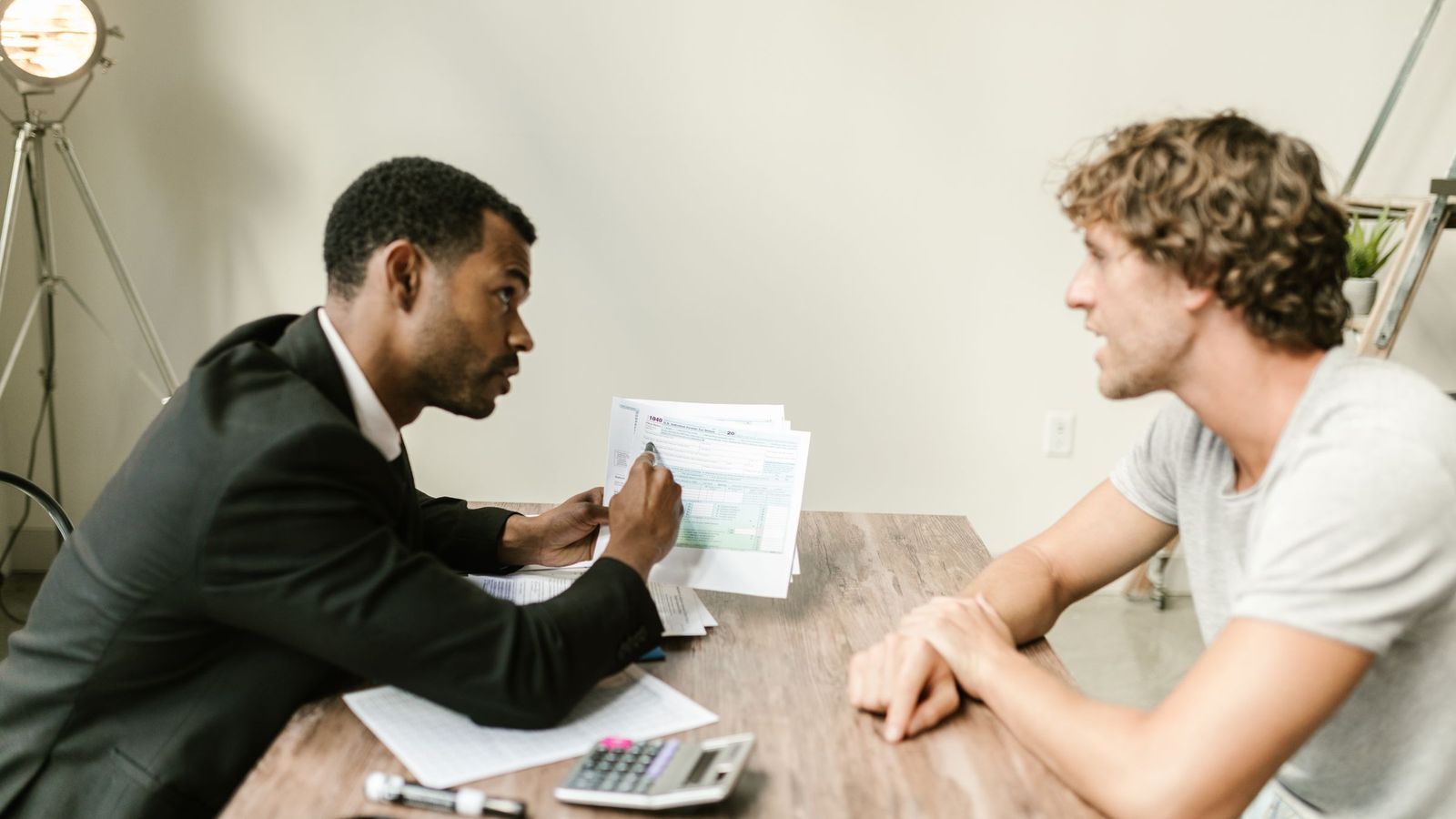 An adviser in a suit goes through printed figures with a client across a wooden desk.