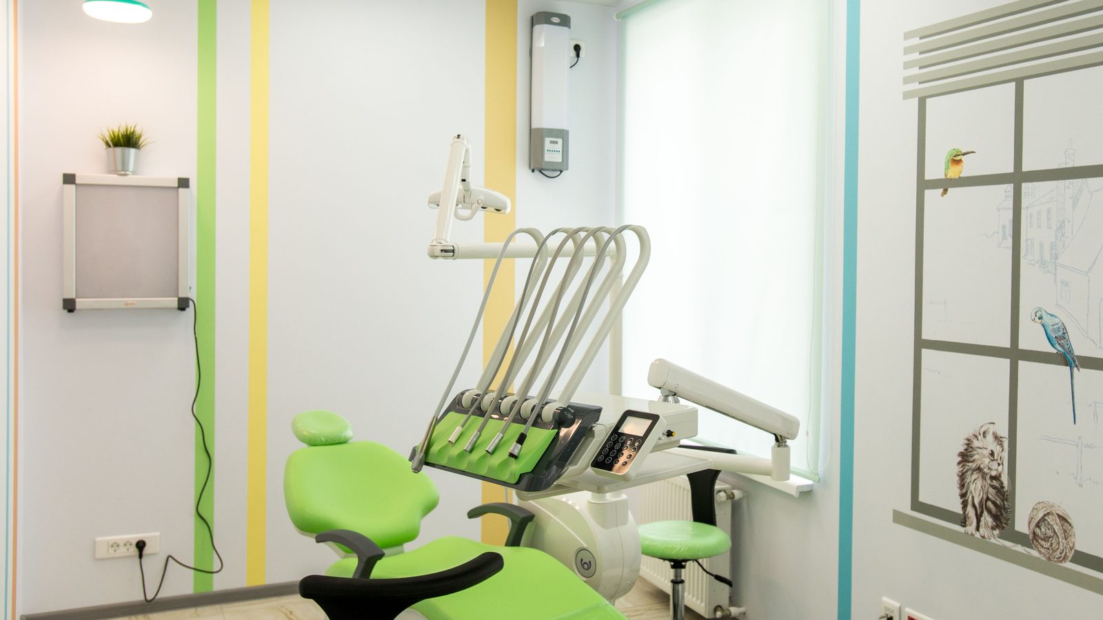An empty dental surgery with a green patient chair by the window.