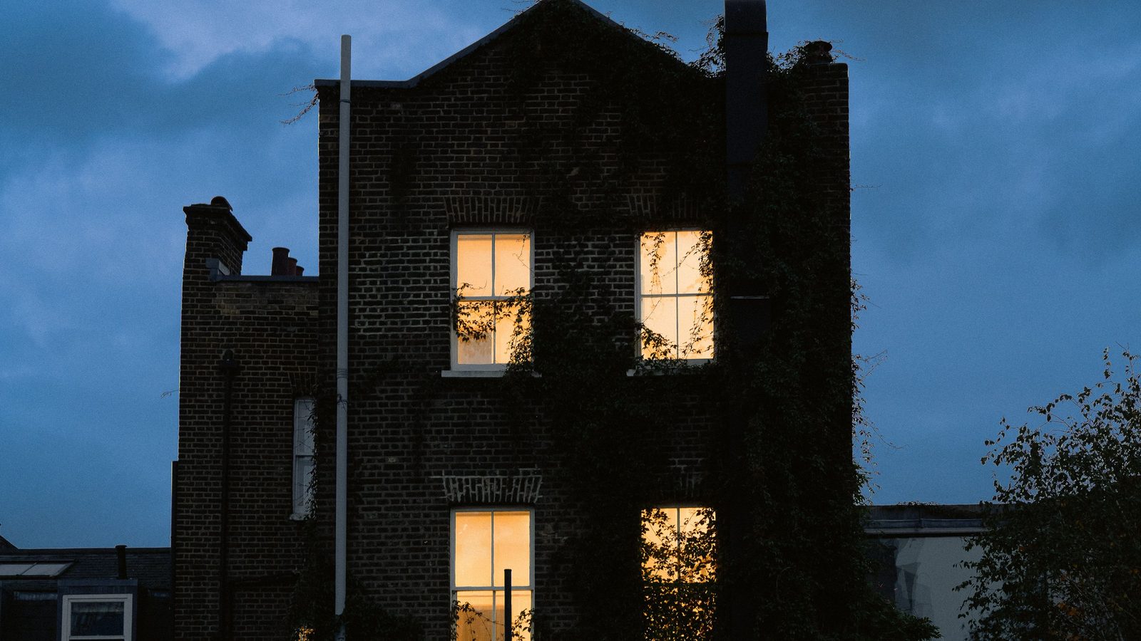 A brick house at dusk with lights on in its windows.