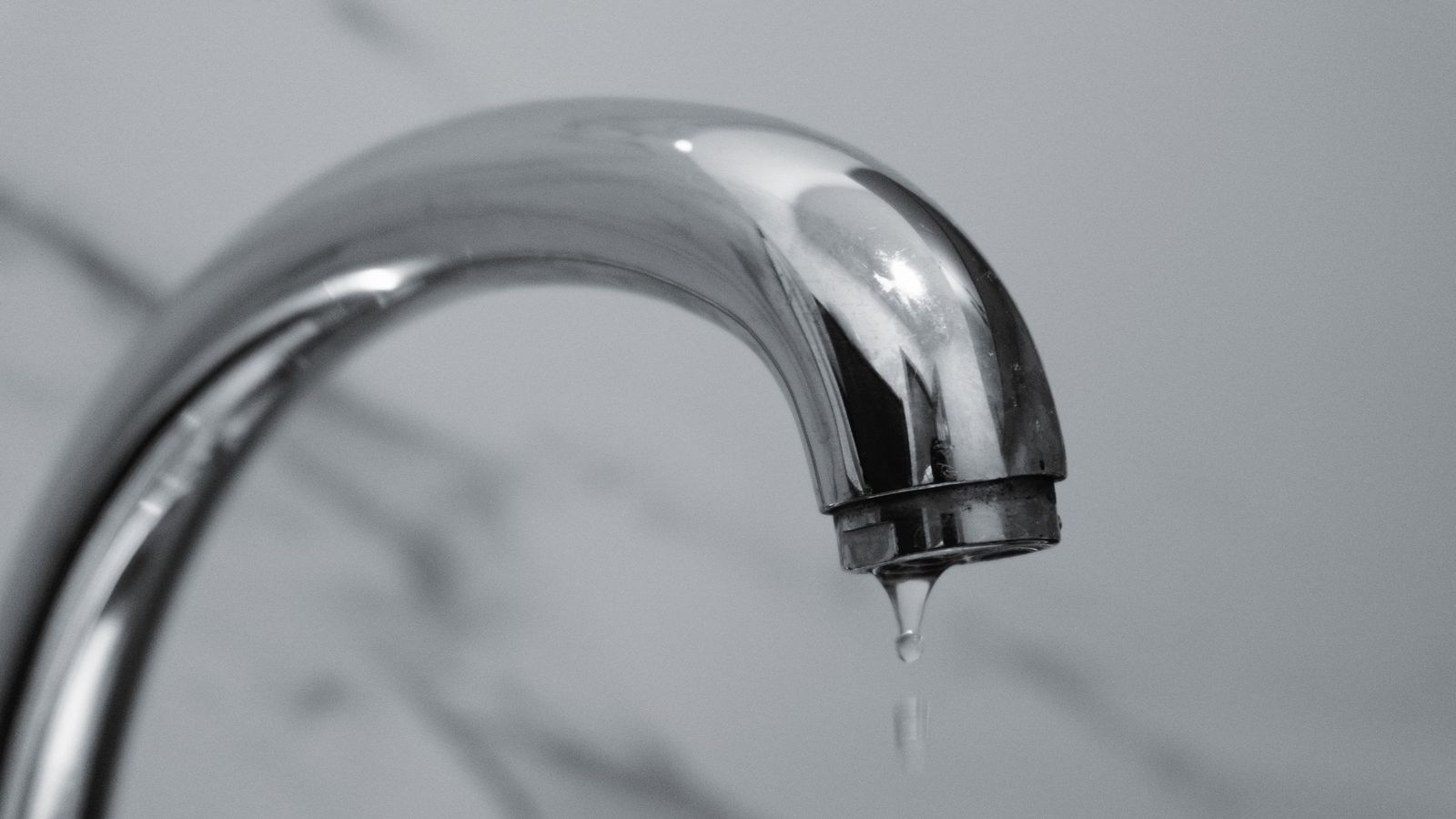 A drop of water falls from a chrome bathroom tap.