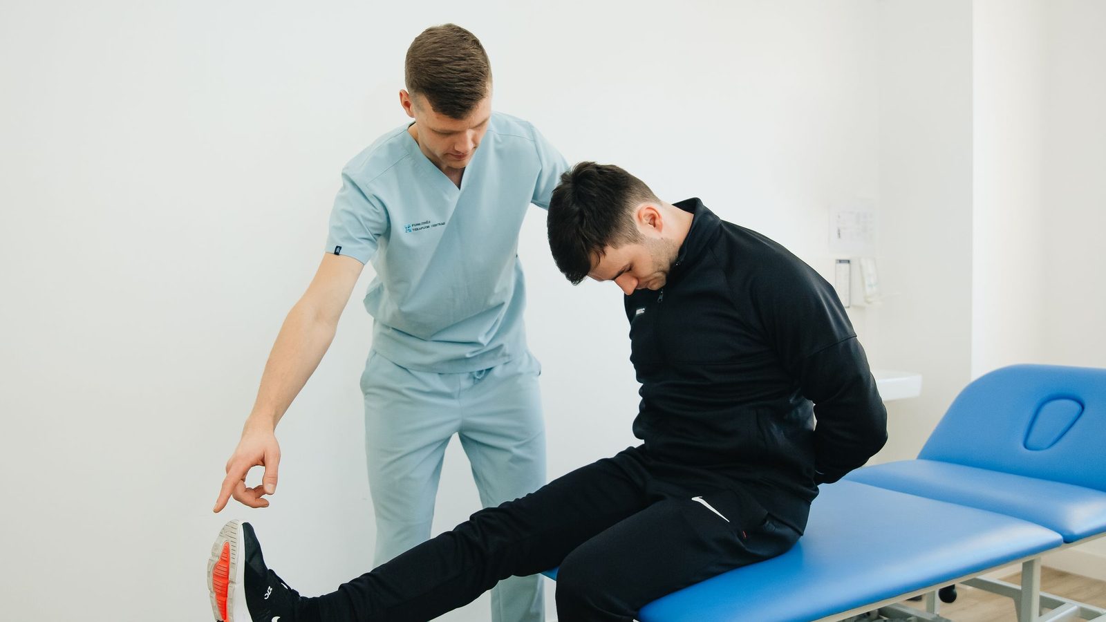 A physiotherapist guides a patient through a stretch beside a treatment couch.