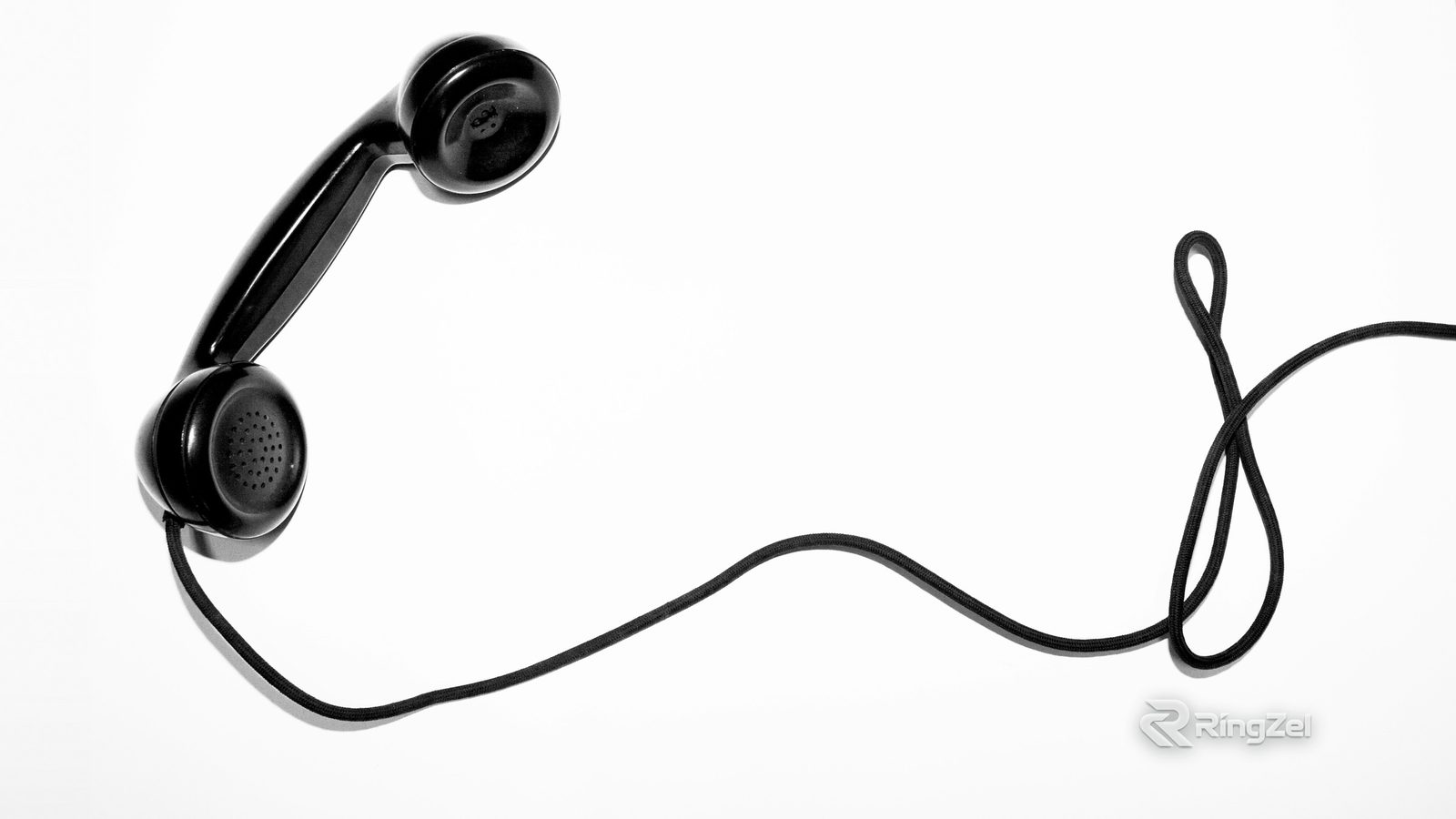A black corded telephone handset lying on a white background, its cord curling across the frame.