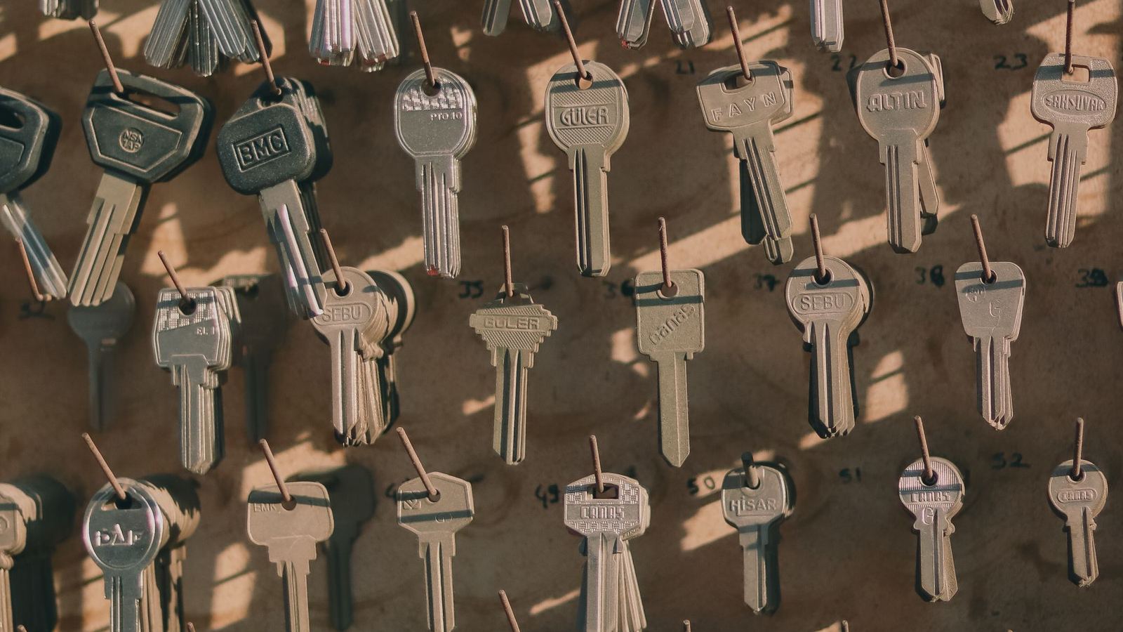 Rows of uncut and cut keys hanging on hooks on a wooden board.