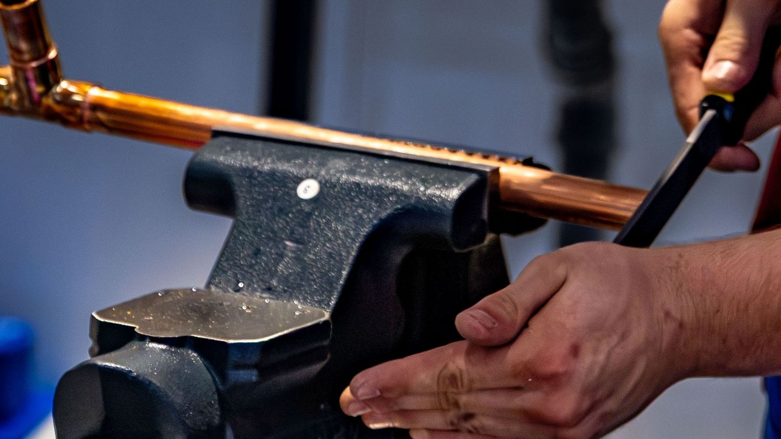A plumber cuts a length of copper pipe held in a bench vice.