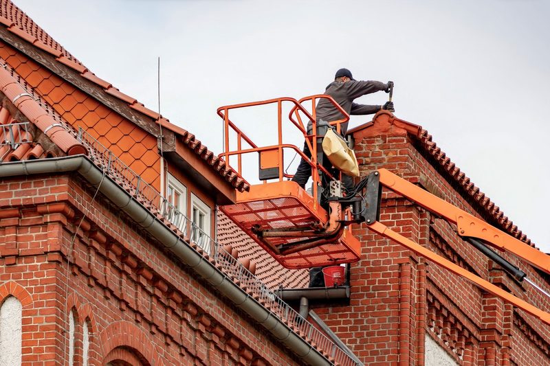 A roofer working from a cherry picker on a brick house
